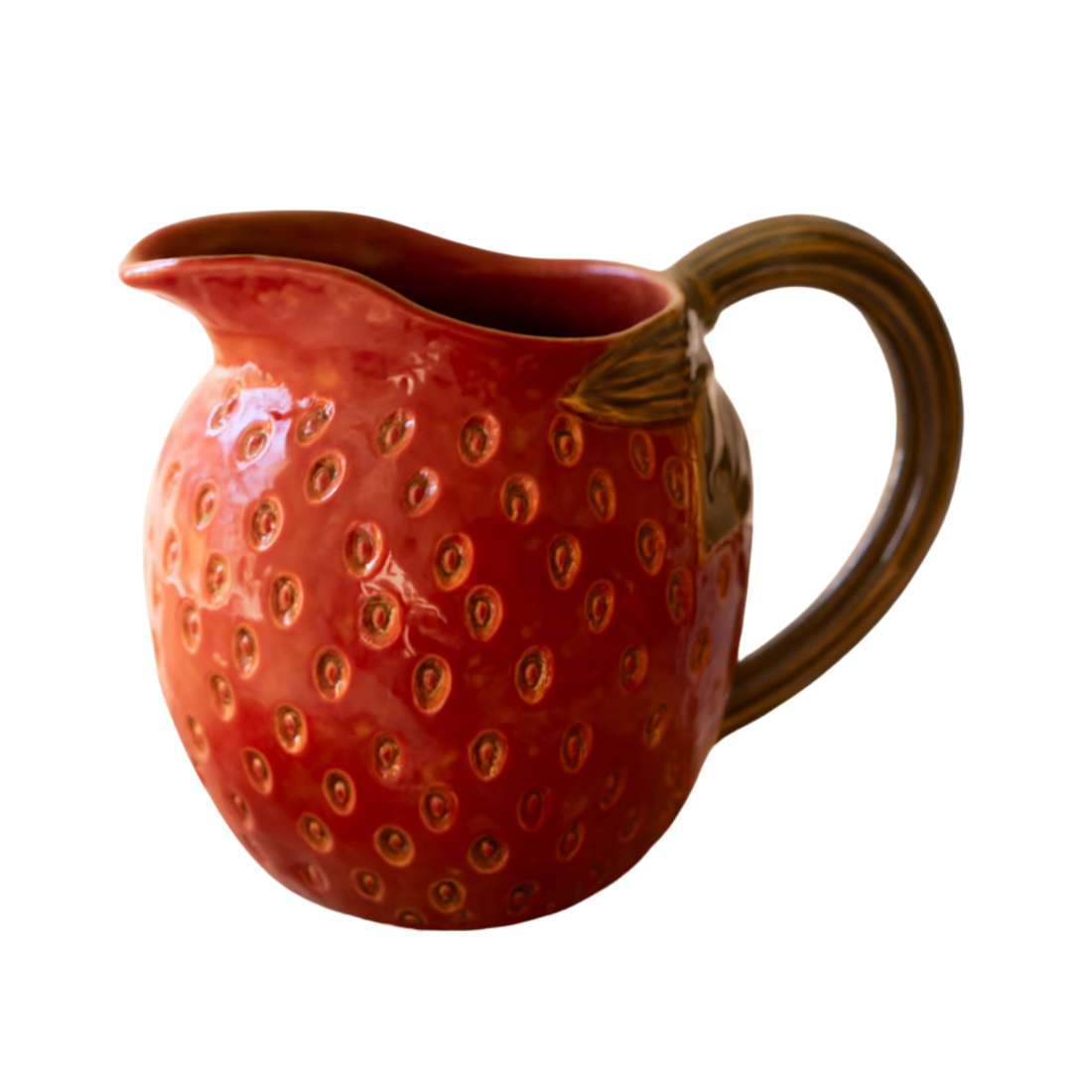 Red ceramic pitcher with strawberry pattern on a marble surface, with gold vases and strawberries in the background.